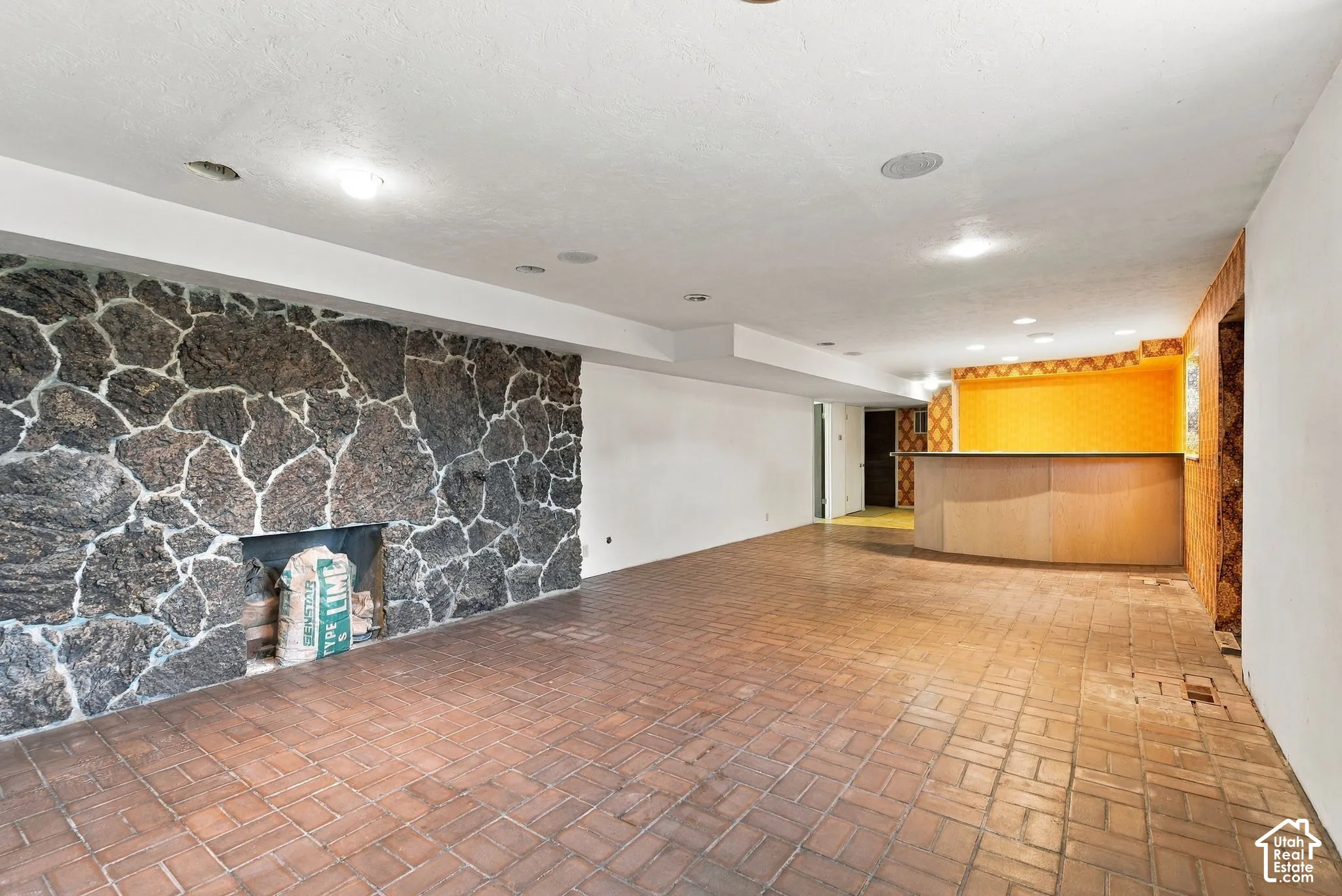 Spacious room featuring brick flooring, a stone fireplace, and a built-in bar with wood-finish cabinetry