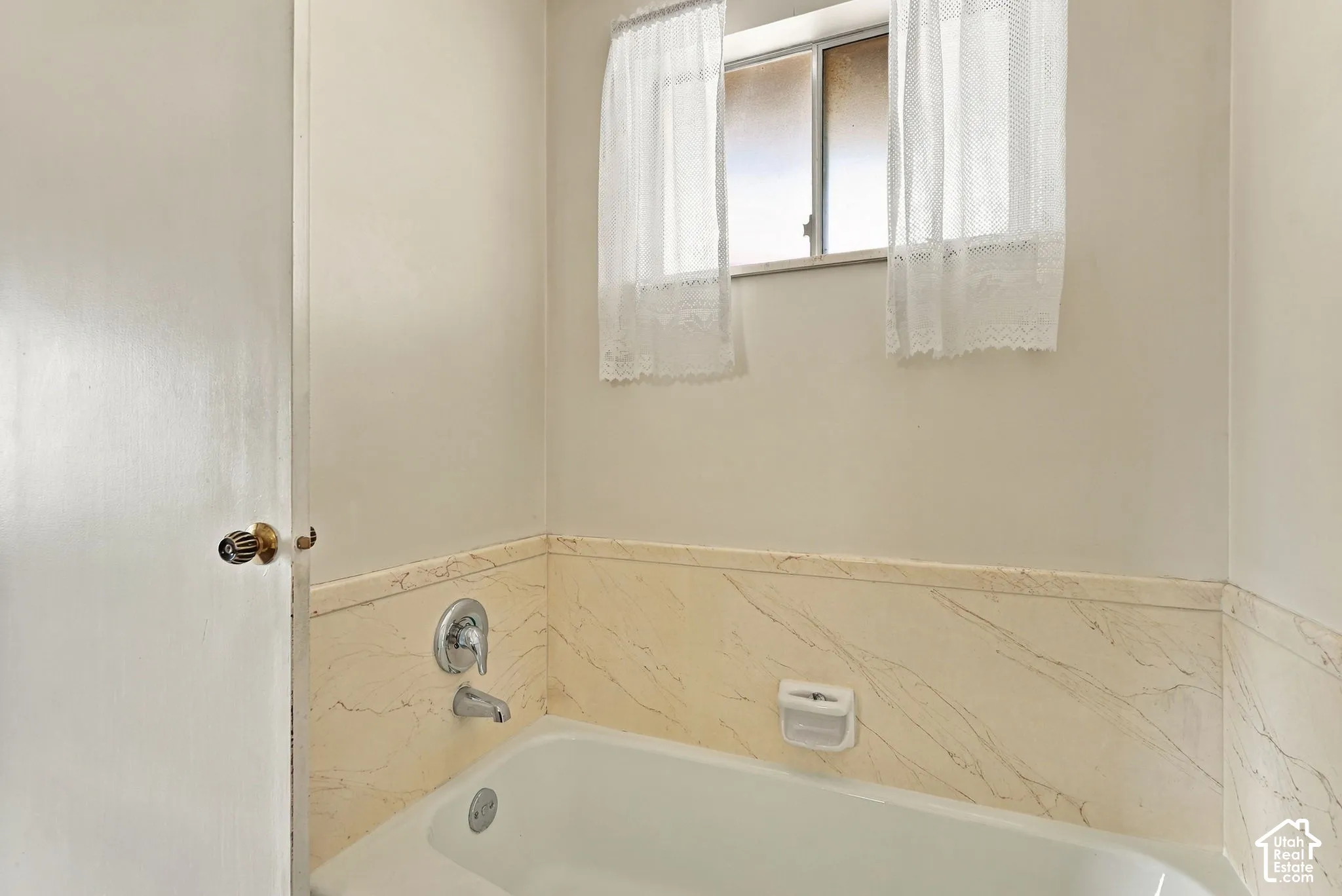 Bathtub with chrome fixtures, tiled surround, and a window for natural light