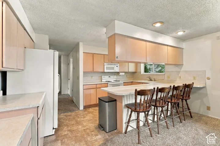 Kitchen featuring wood-finish cabinetry, white appliances, recessed lighting, and a breakfast bar