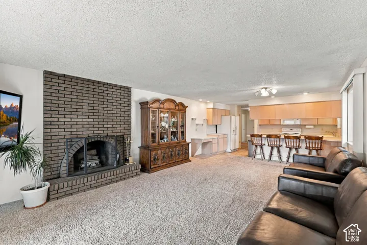 Spacious open-concept living area featuring a brick fireplace with wood-burning insert, neutral carpet flooring, and leather seating
