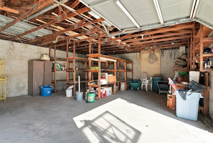 Concrete flooring, exposed wood beam ceiling, block wall construction, built-in open shelving, and a roll-up garage door