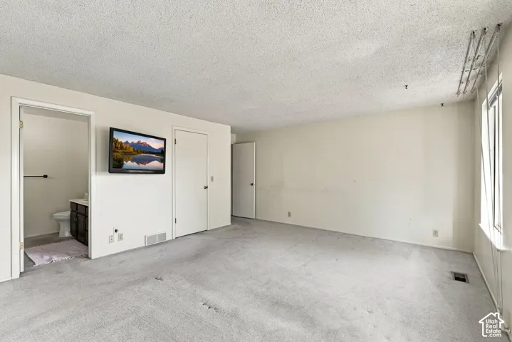 Carpeted room with a textured ceiling, featuring a window and a separate room with a toilet and vanity
