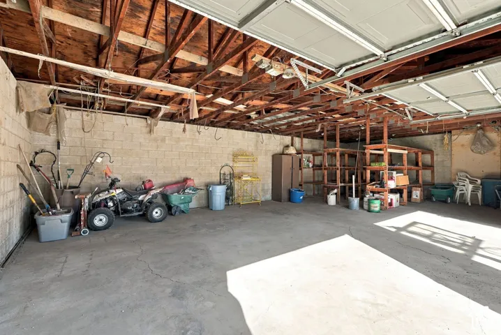 Open garage space with concrete flooring, exposed wood beam ceiling, and concrete block walls