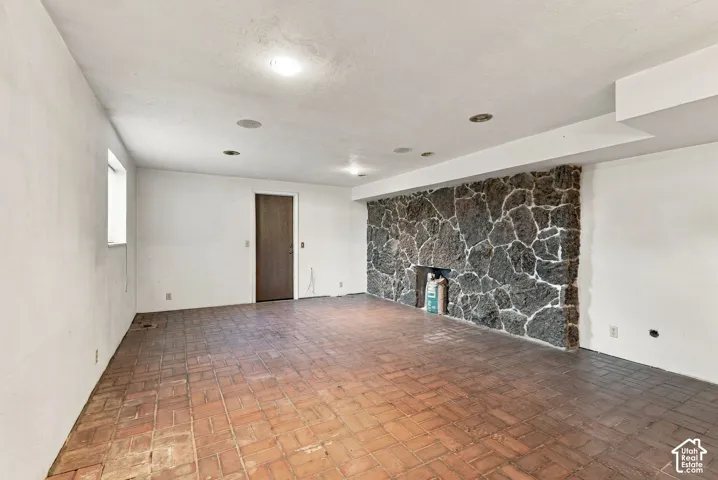Stone accent wall with fireplace, exposed brick flooring, recessed ceiling lighting, and a single window