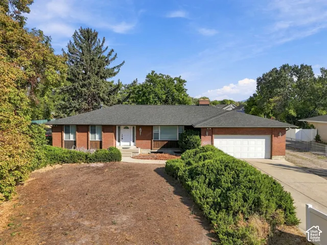 Brick exterior, attached garage, paved driveway, mature landscaping, and a composite shingle roof