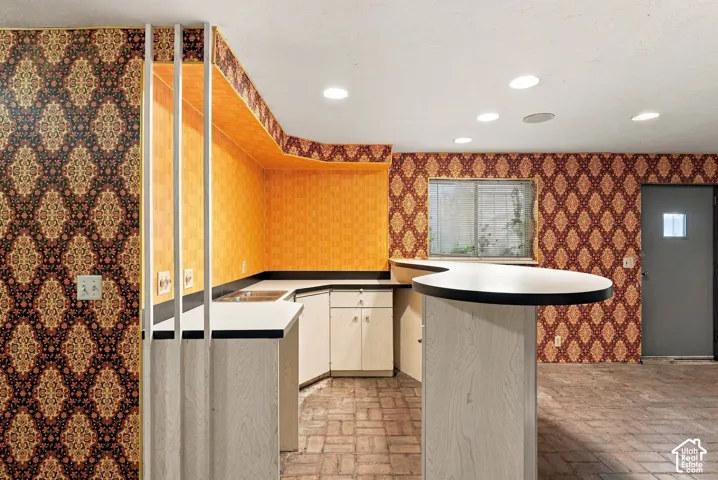 Built-in bar with white countertop and black trim, recessed ceiling lighting, brick-patterned flooring, and a window with security bars