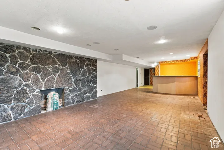 Spacious room featuring brick flooring, a stone fireplace, and a built-in bar with wood-finish cabinetry