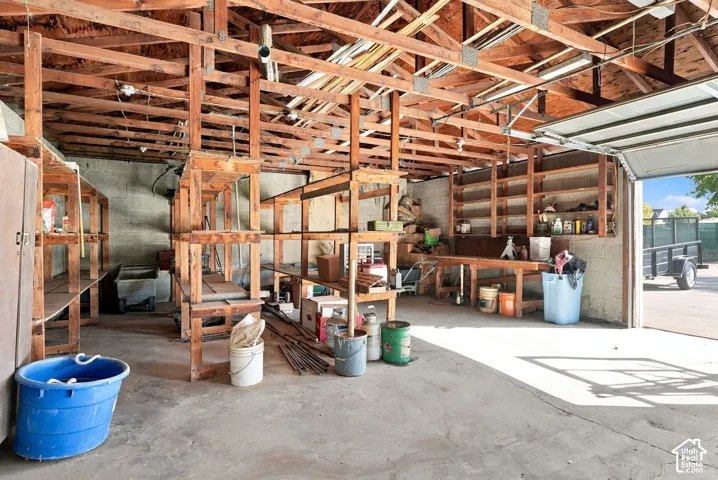 Exposed wood beam ceiling, concrete flooring, built-in wooden shelving, integrated workbench, and overhead fluorescent lighting
