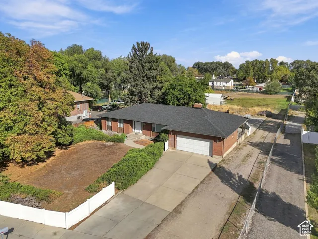 Brick exterior with white trim, attached garage, dark shingle roof, and established landscaping