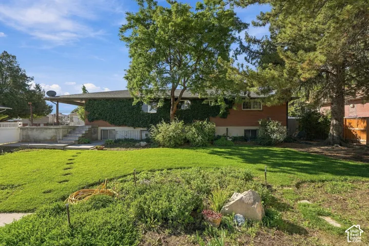Brick exterior with extensive green climbing foliage, mature trees, a covered patio area, and a terraced lawn with stepping stones