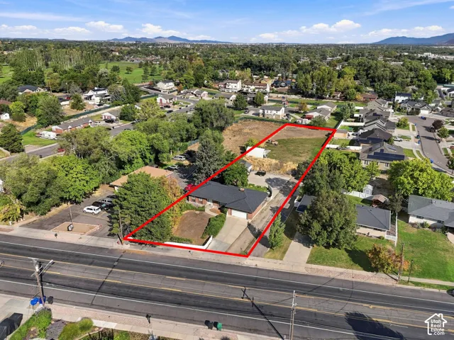 Expansive property featuring a single-story residence with a dark roof, a concrete driveway, and a large undeveloped lot