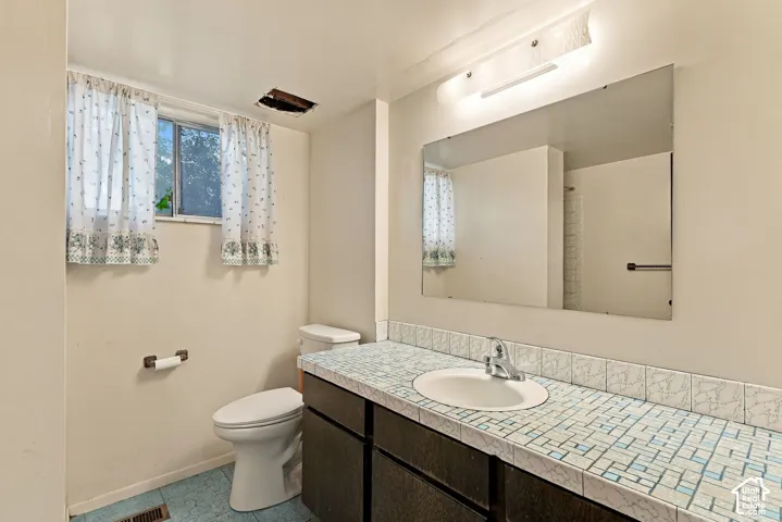 Vanity with integrated sink, mosaic tile countertop, and large wall-mounted mirror