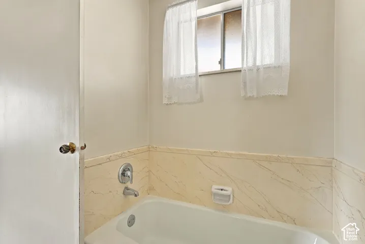 Bathtub with chrome fixtures, tiled surround, and a window for natural light