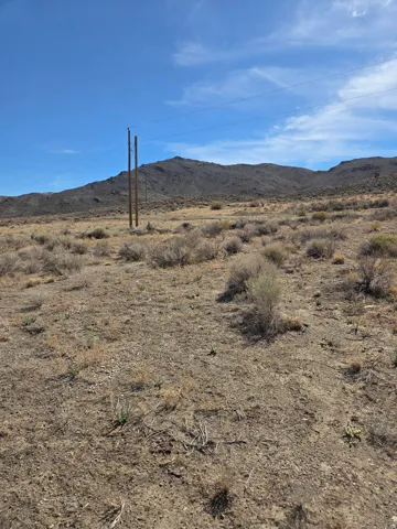 Expansive land parcel featuring natural desert vegetation, distant mountains, and utility poles