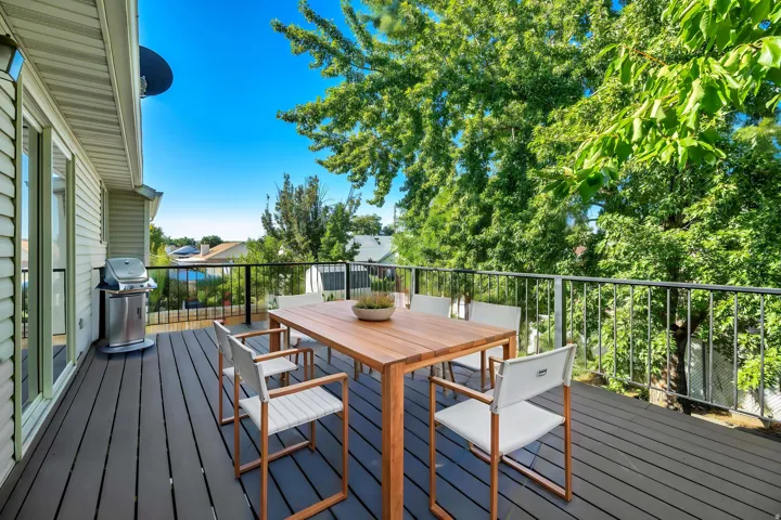 Expansive outdoor deck featuring dark composite decking, sleek metal railings, and mature surrounding trees
