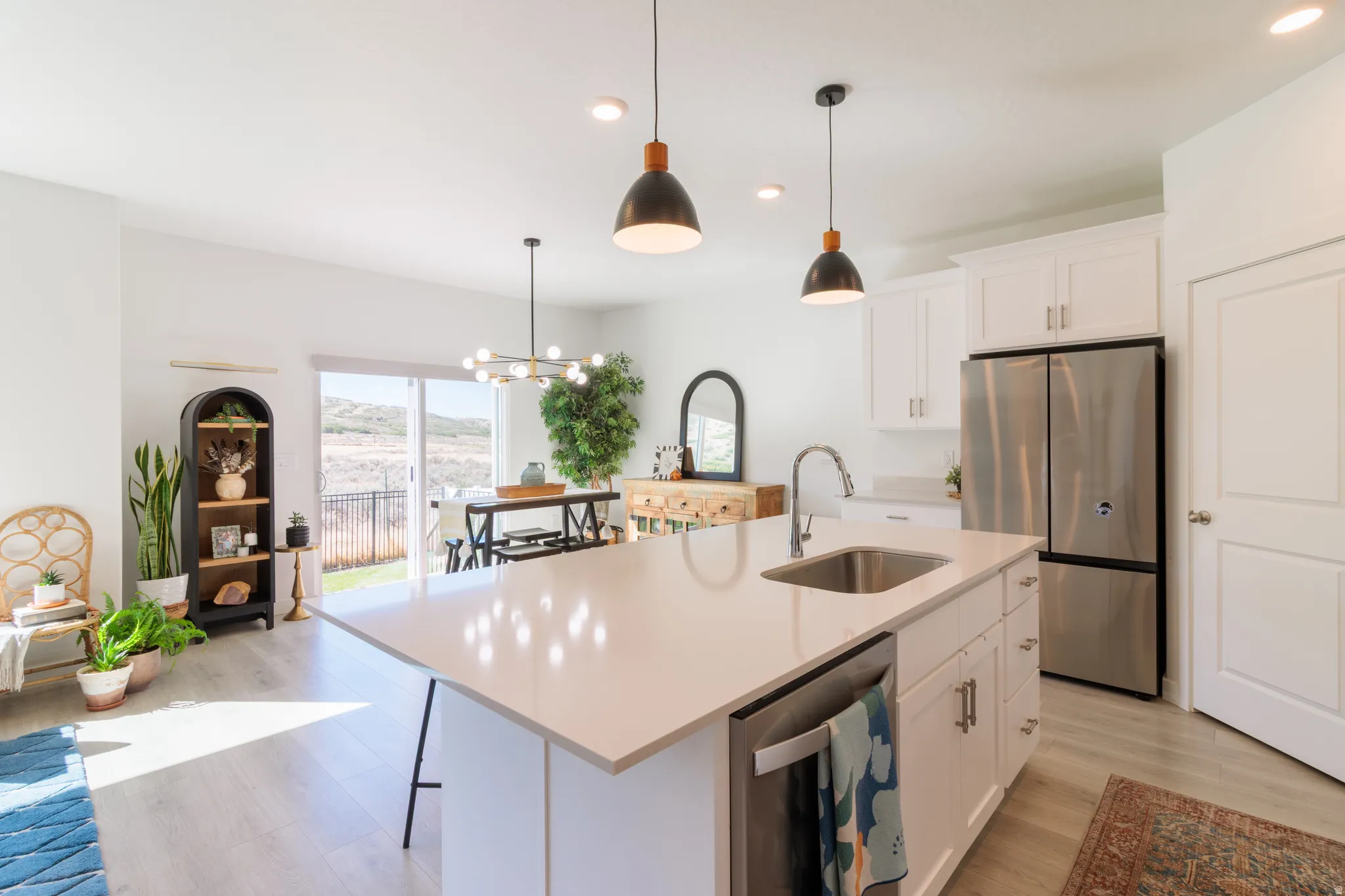 Kitchen island with integrated sink, white cabinetry, stainless steel appliances, and wood-finish flooring