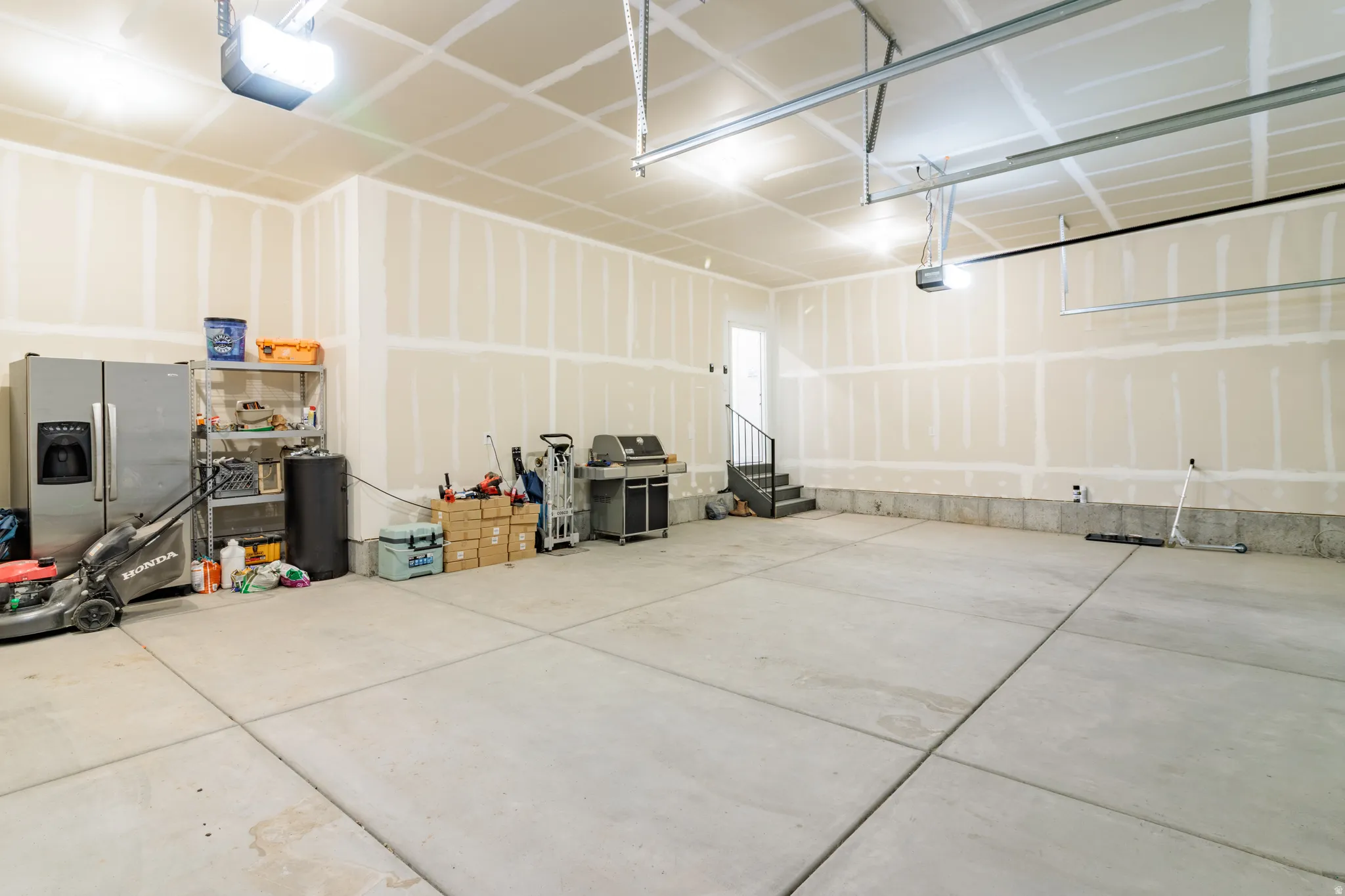 Spacious garage with concrete flooring, automatic garage door openers, and a built-in staircase with a metal railing