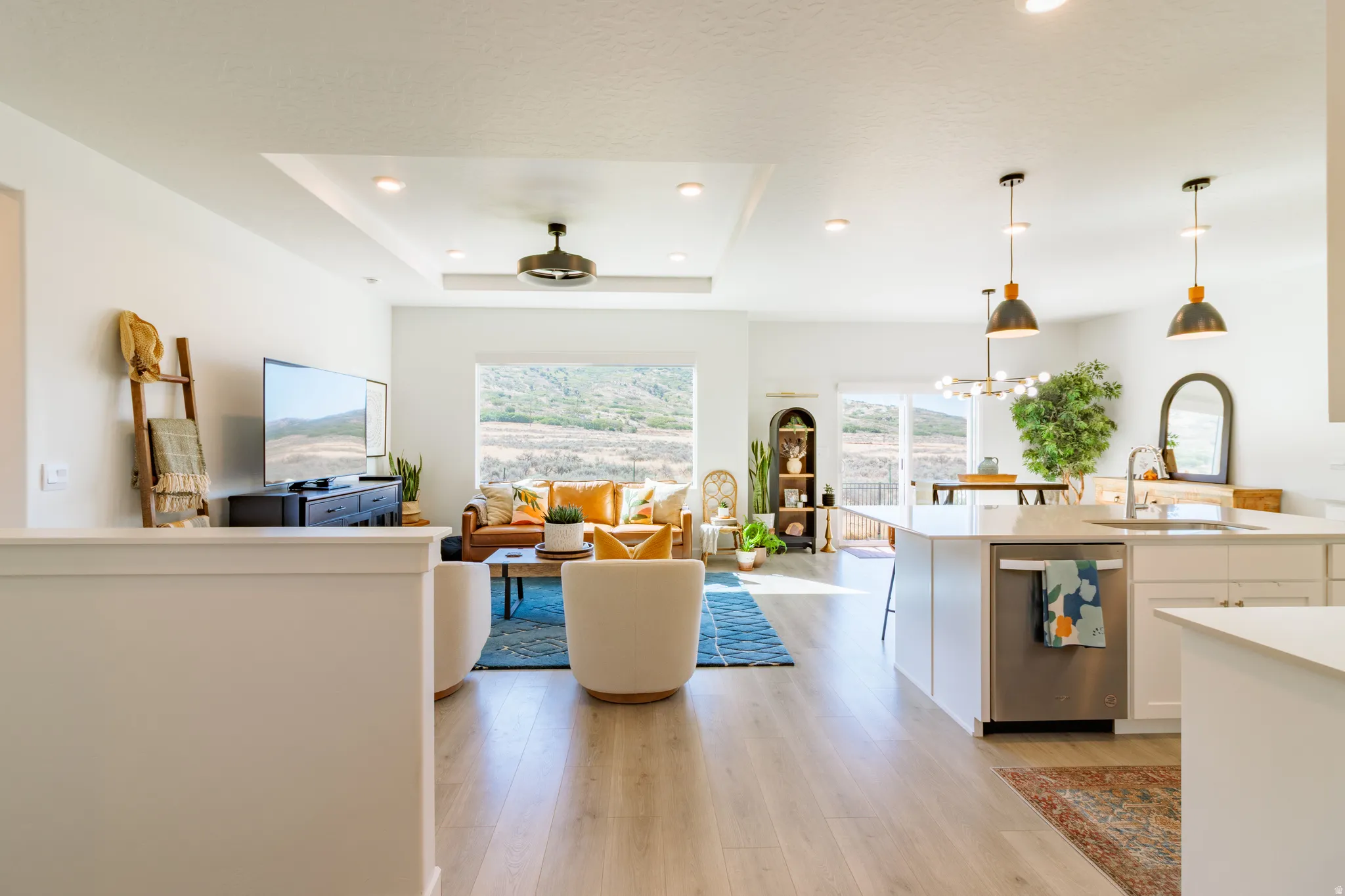 Open-concept living space with light wood-finish flooring, recessed lighting, and a tray ceiling with a built-in fan