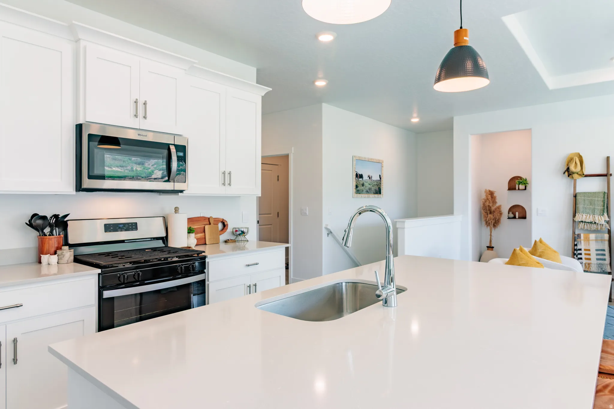 White shaker cabinetry with crown molding, stainless steel microwave, gas range with stainless steel hood, undermount sink with gooseneck faucet, and white countertops