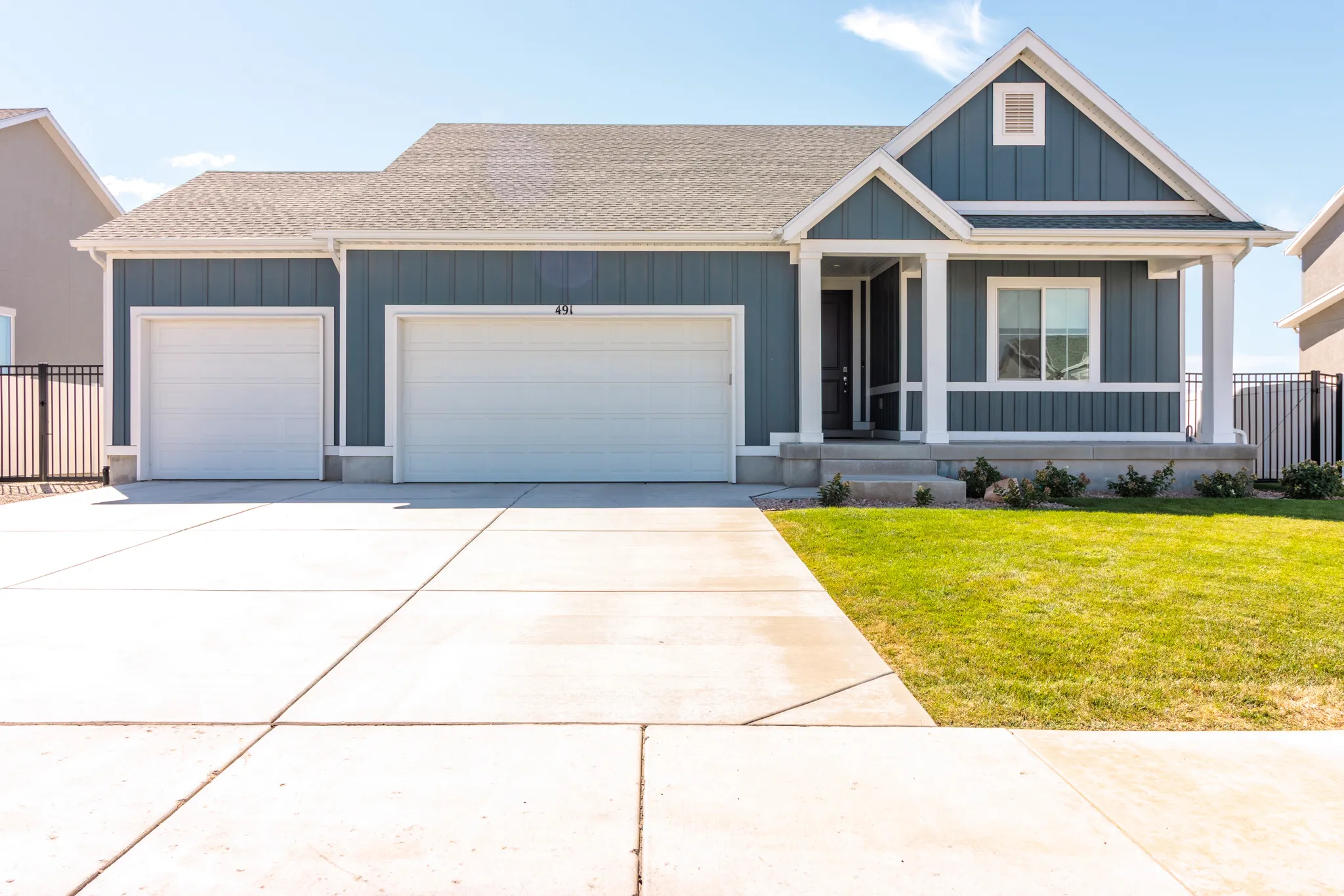 Blue siding exterior with white trim, two attached garage doors, a covered porch entry, a front lawn, and a concrete driveway