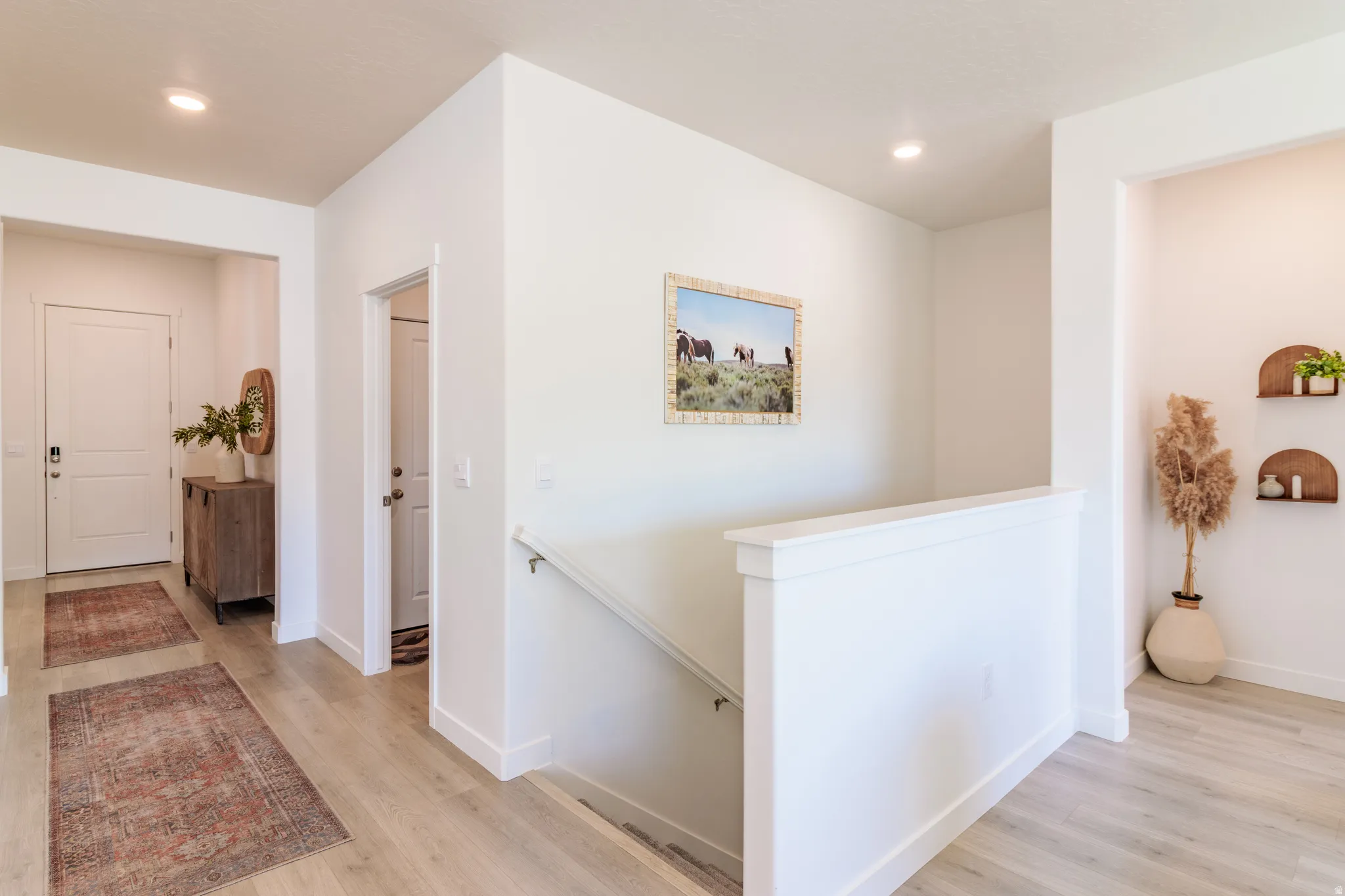 Light wood-finish flooring throughout, white painted walls, recessed ceiling lighting, two panel interior doors, and a white staircase railing