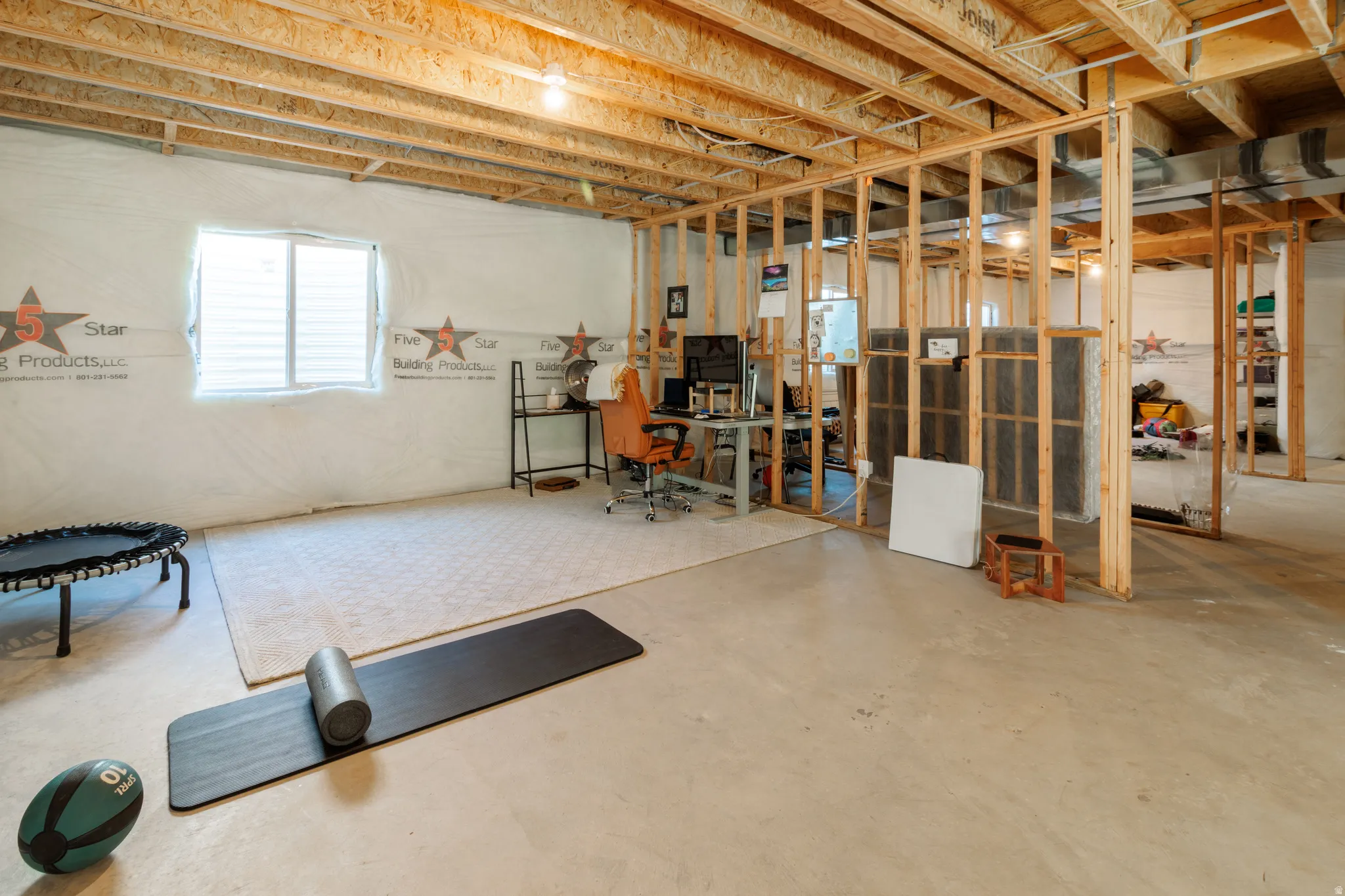 Unfinished basement with exposed wood framing, concrete flooring, and an egress window