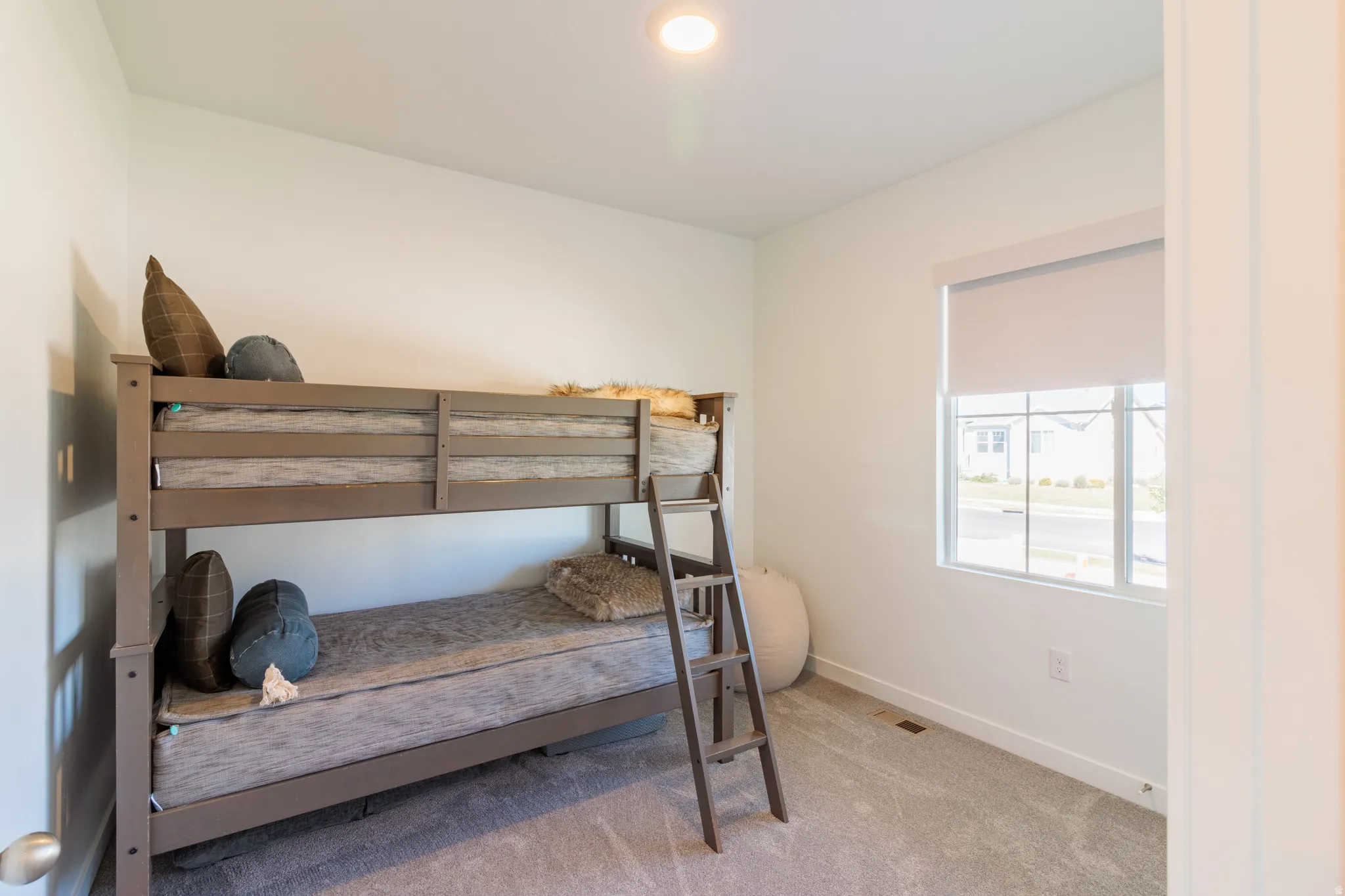Recessed ceiling lighting, a window with roller shade, and neutral-toned carpeting