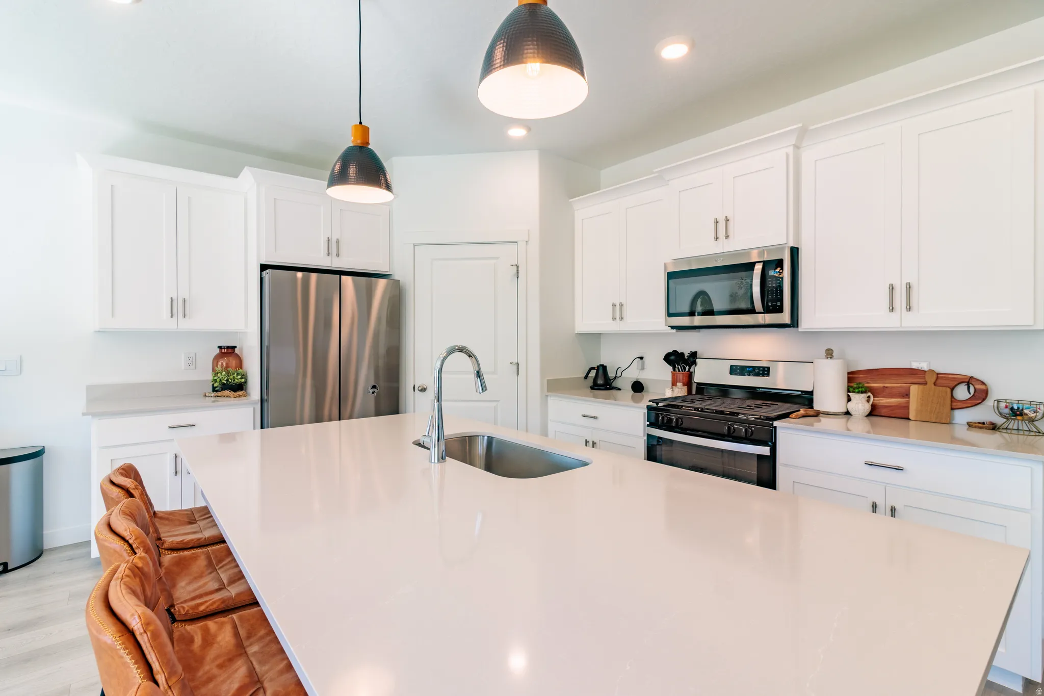 Kitchen featuring a large central island with an undermount sink, white cabinetry with silver-tone hardware, stainless steel appliances, and recessed lighting