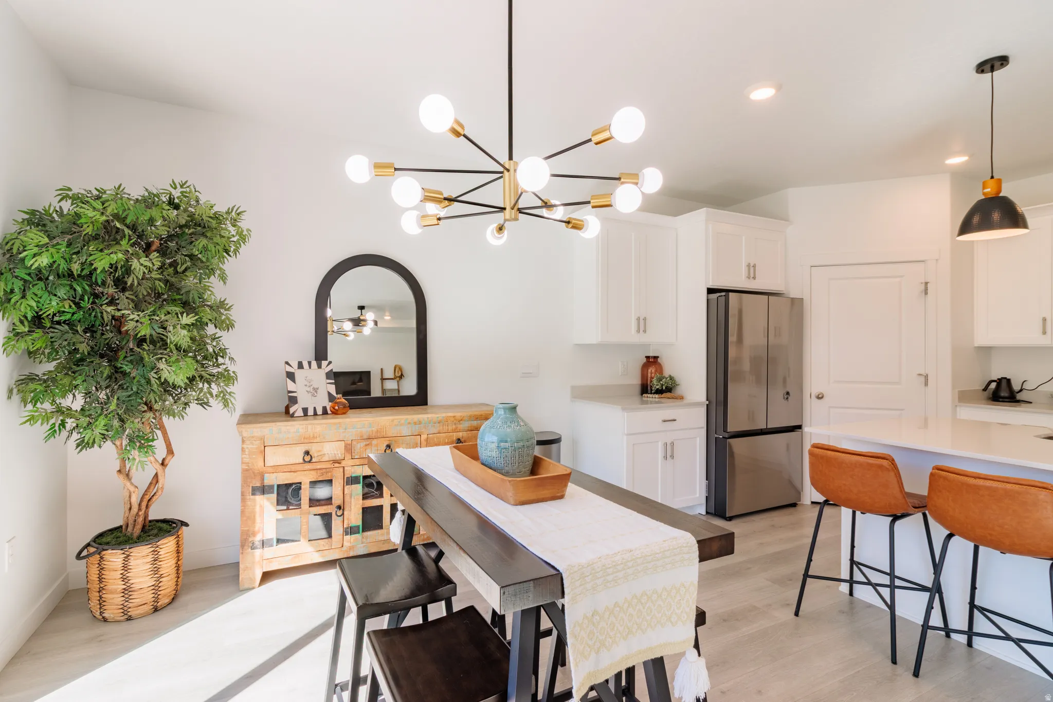 Open concept living area featuring a modern sputnik chandelier, light wood-finish flooring, white kitchen cabinetry, stainless steel refrigerator, and a kitchen island with seating