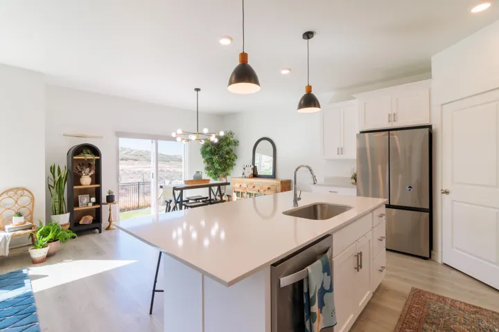 Kitchen island with integrated sink, white cabinetry, stainless steel appliances, and wood-finish flooring