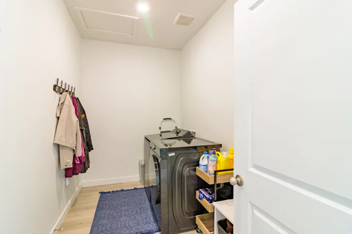 Recessed lighting illuminates this utility space, featuring light wood-finish flooring and a functional coat rack
