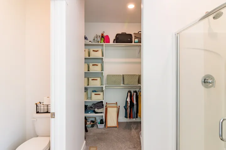Built-in closet shelving, integrated hanging rods, recessed lighting, and a white shower enclosure with chrome fixtures