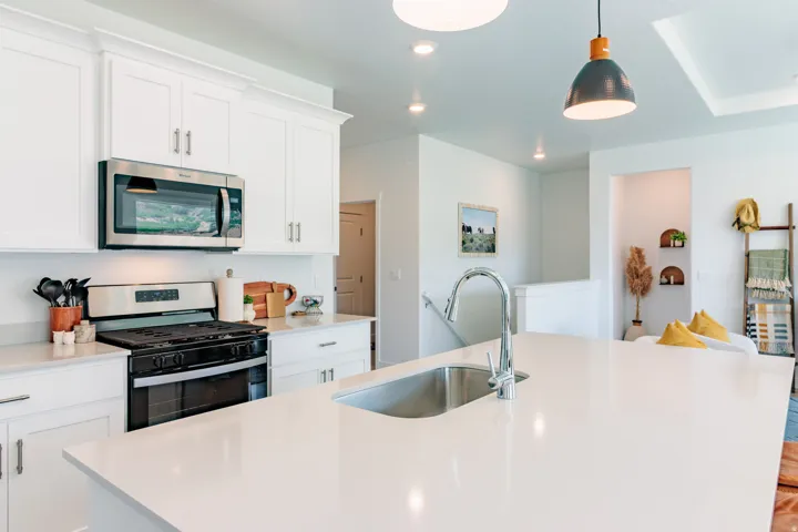 White shaker cabinetry with crown molding, stainless steel microwave, gas range with stainless steel hood, undermount sink with gooseneck faucet, and white countertops