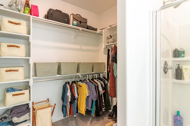 White built-in shelving, chrome hanging rods, and a glass-enclosed shower with a built-in shelf
