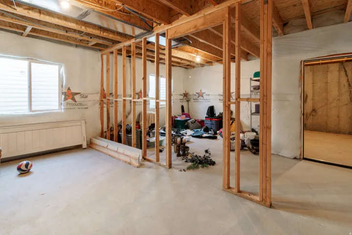 Unfinished lower level with exposed ceiling joists, framed interior walls, concrete flooring, and windows providing natural light