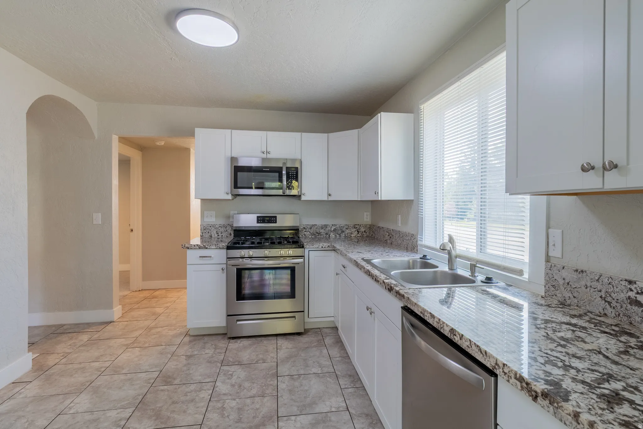 Tile flooring, white cabinetry, stainless steel appliances, dual basin sink, and stone-finish countertops