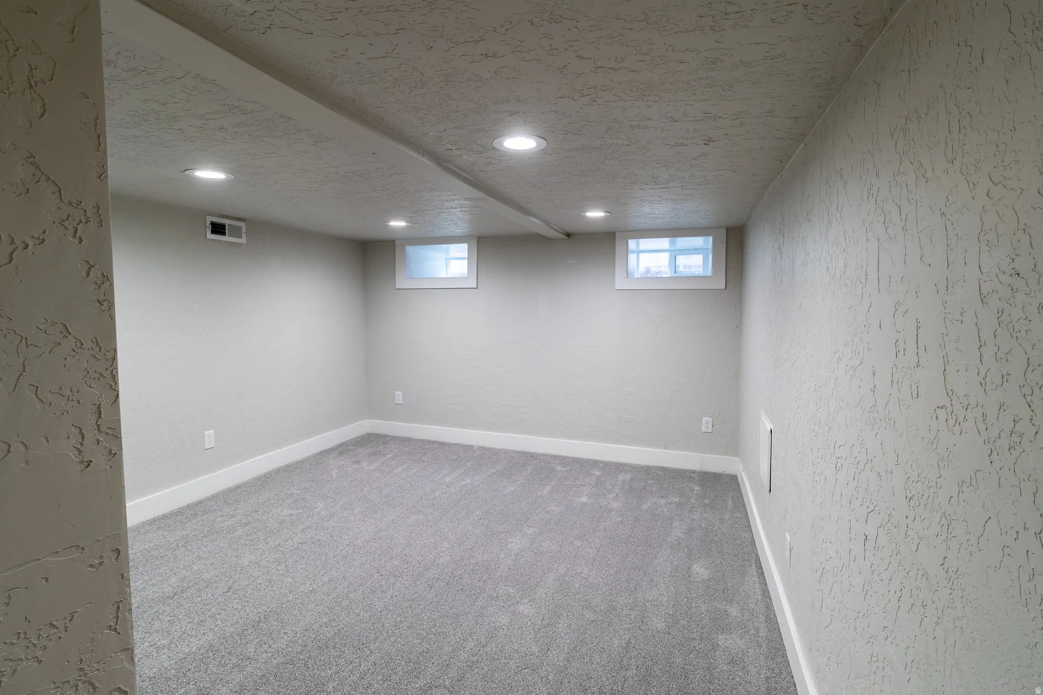 Recessed lighting, light gray carpeting, neutral wall color, two windows, and textured wall finish