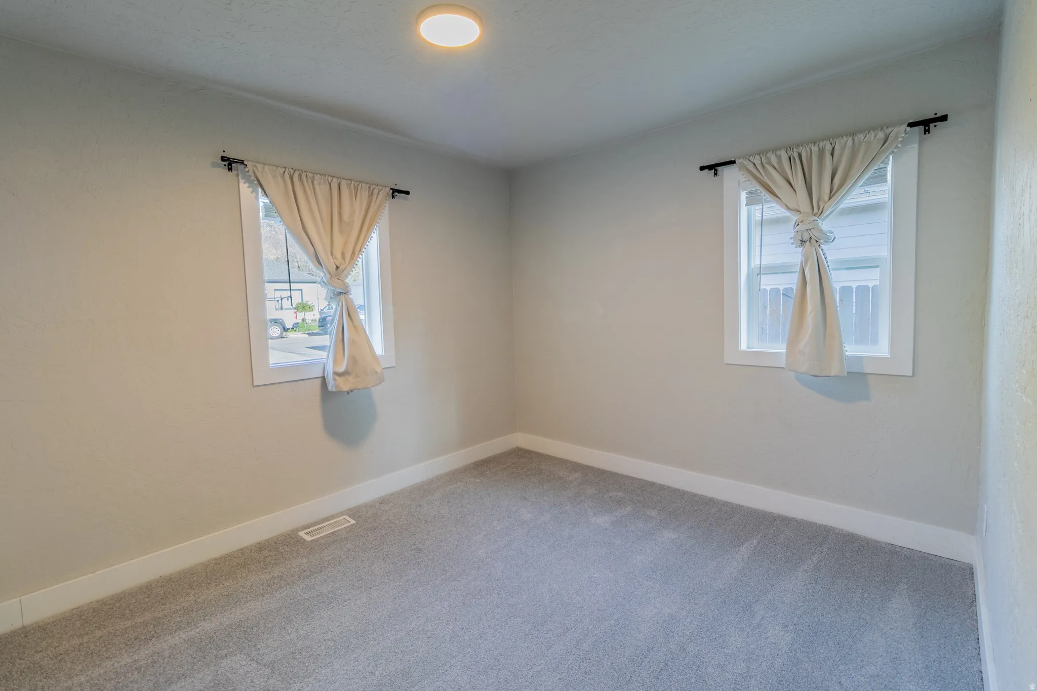 Recessed ceiling light, two windows with white trim, light gray walls, and gray carpet flooring
