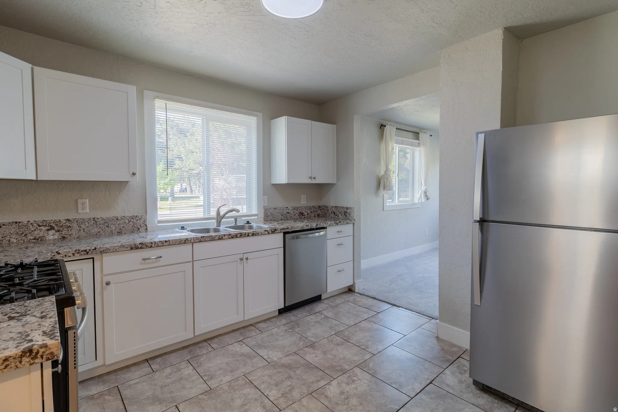 Kitchen featuring white cabinetry, a double basin sink, stainless steel appliances, and tile flooring