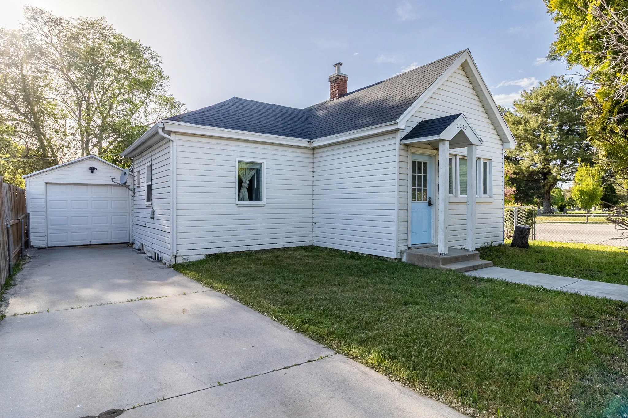 White siding exterior with a light blue entry door, concrete driveway, detached garage, and a sloped roof