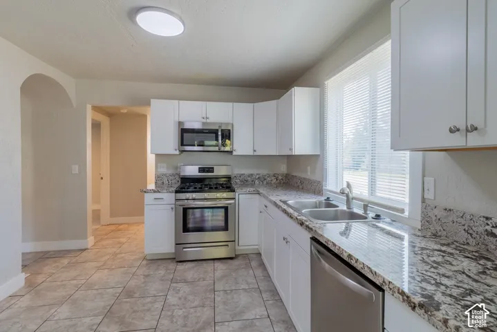 Tile flooring, white cabinetry, stainless steel appliances, dual basin sink, and stone-finish countertops
