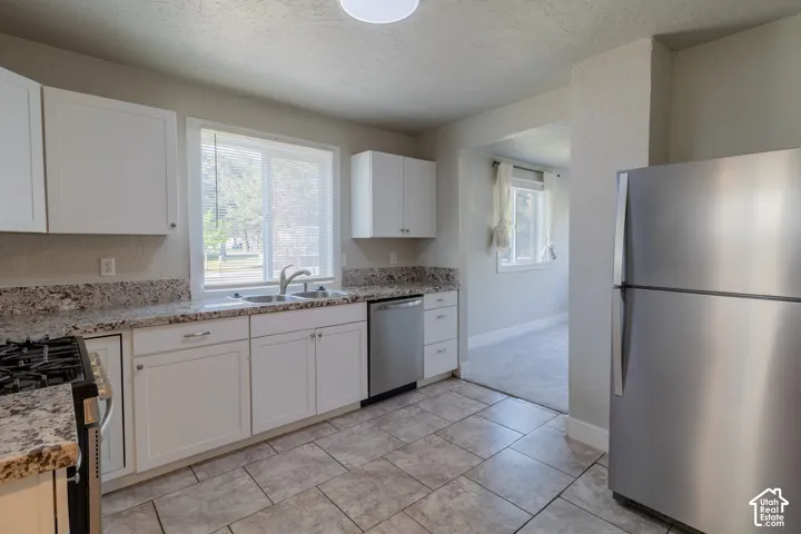 Kitchen featuring white cabinetry, a double basin sink, stainless steel appliances, and tile flooring