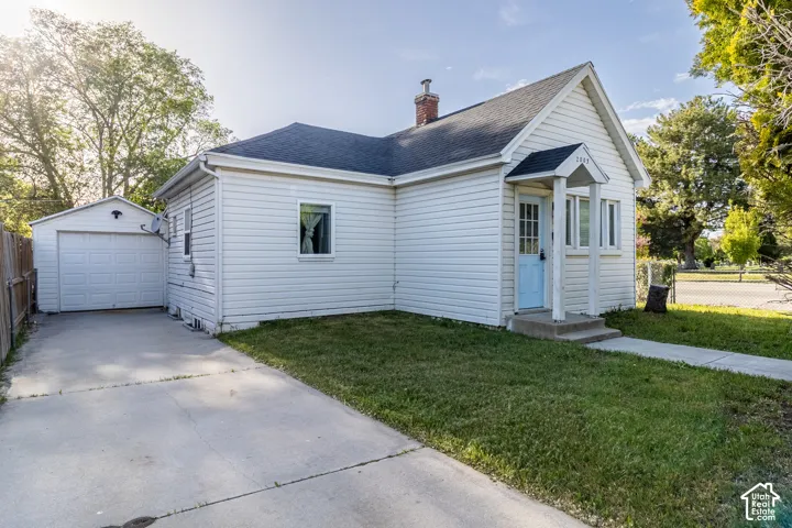 White siding exterior with a light blue entry door, concrete driveway, detached garage, and a sloped roof