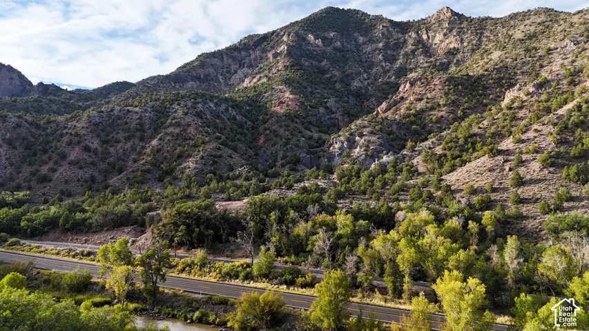 Mountainous terrain with natural rock formations, scattered trees, and a visible roadway