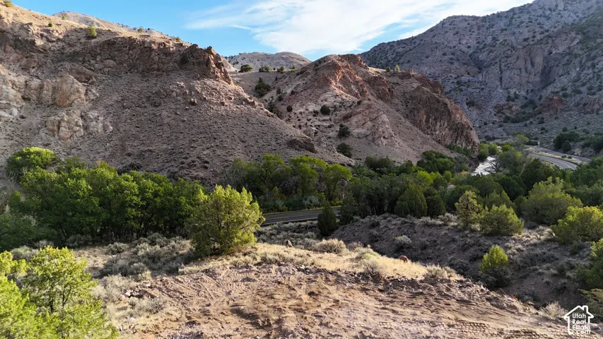 Mountainous terrain featuring natural rock formations, abundant green foliage, a winding river, and a paved road
