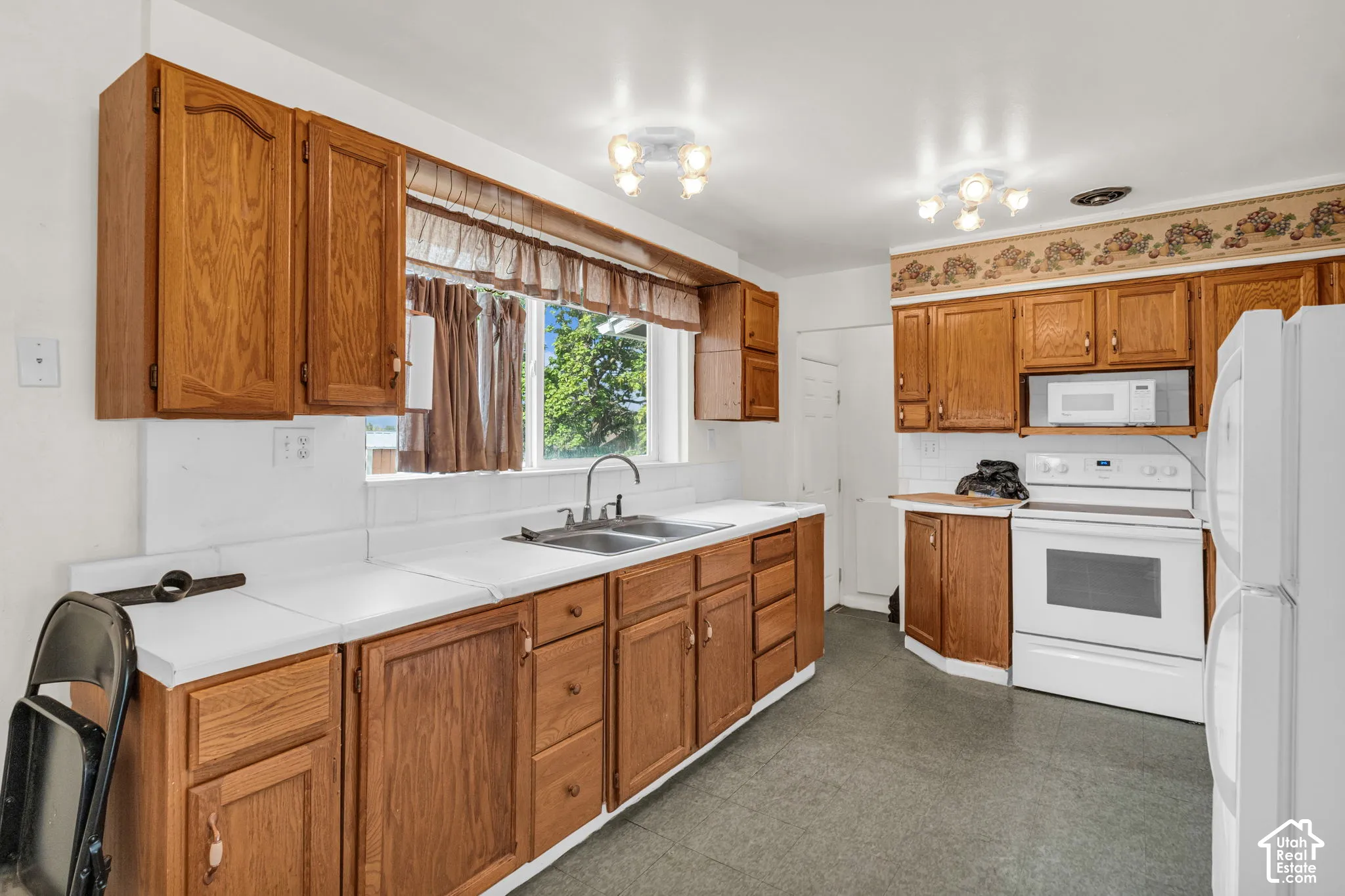 Kitchen featuring wood-finish cabinetry, a double basin sink, and a white appliance suite