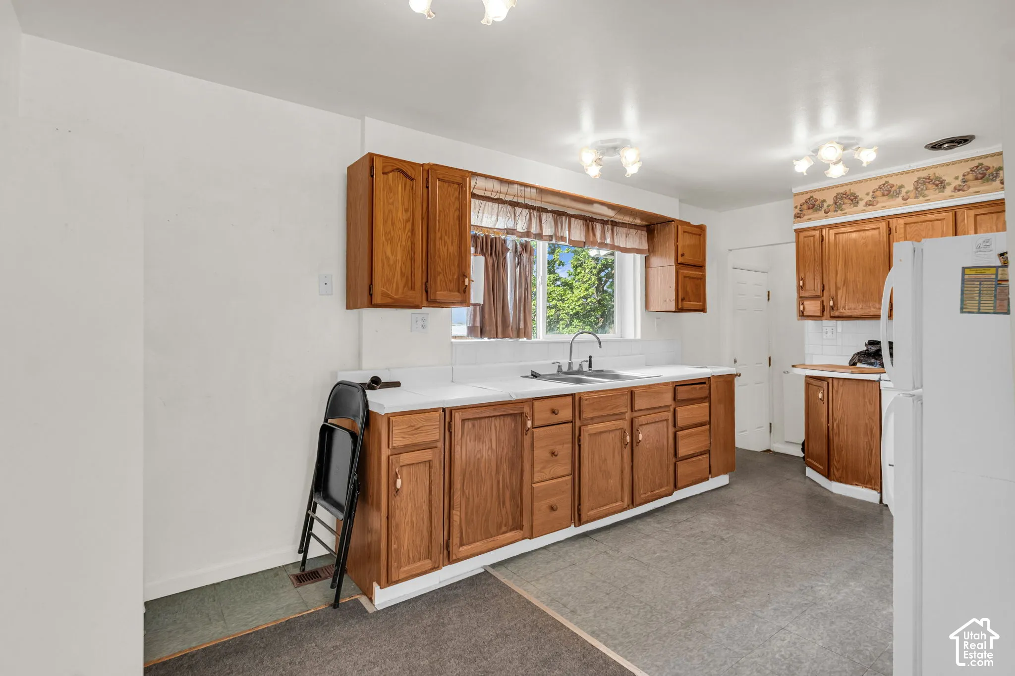 Kitchen featuring wood cabinetry, white countertops, a double-basin sink, and white tile backsplash