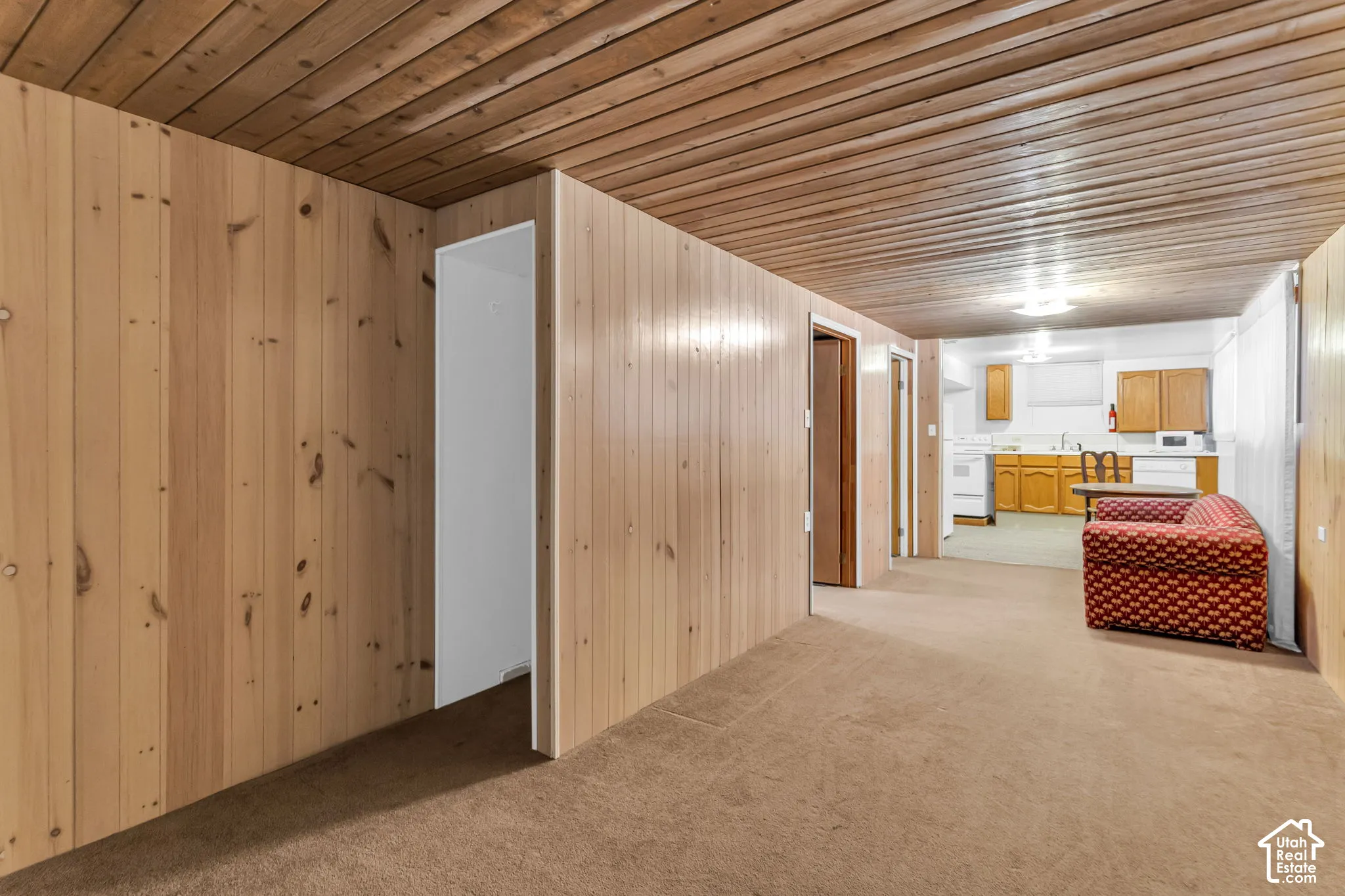 Wood paneling, wood-finish ceiling, brown carpet flooring, recessed lighting, and a partial kitchen with wood cabinetry