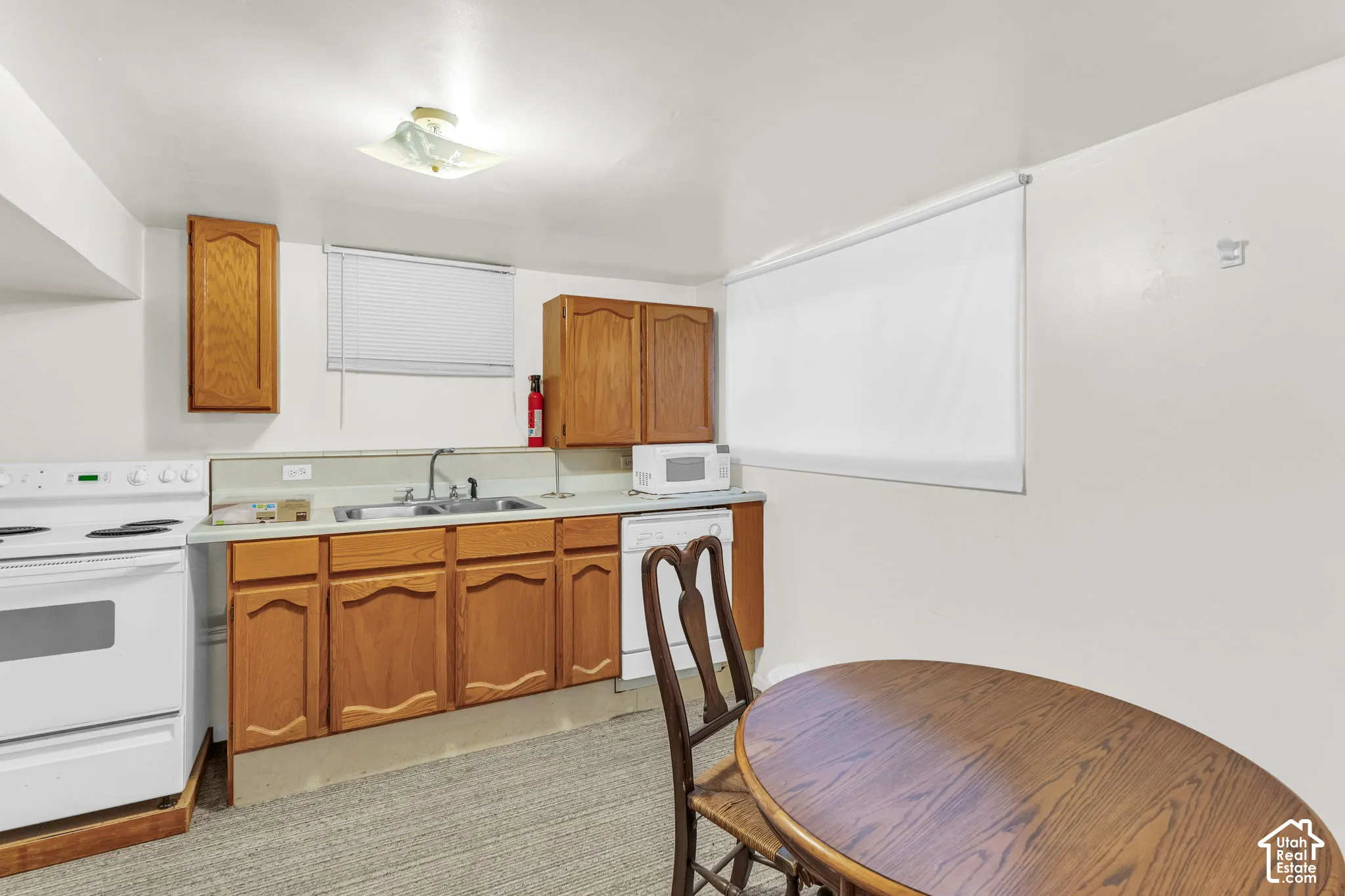 Kitchenette featuring wood-finish cabinetry, a stainless steel sink, and white appliances including a range and dishwasher