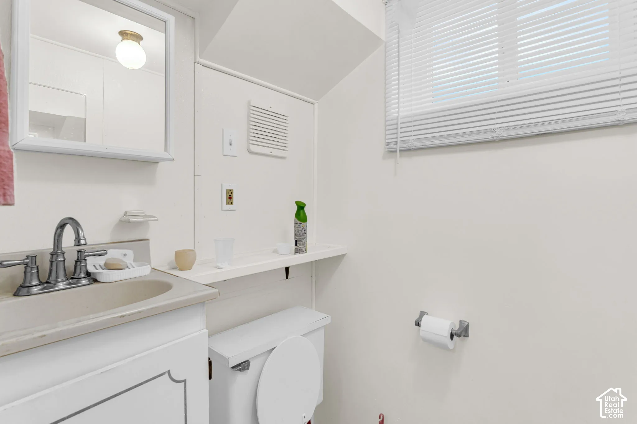 Vanity with integrated sink, wall-mounted mirror, window with blinds, toilet, and flush-mount ceiling light